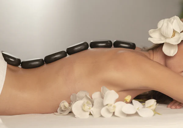 Massage aux pierres chaudes sur le dos, entouré de fleurs blanches