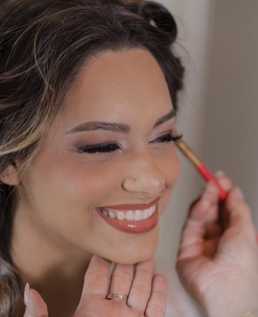 Une mariée souriante, les yeux fermés, pendant son maquillage