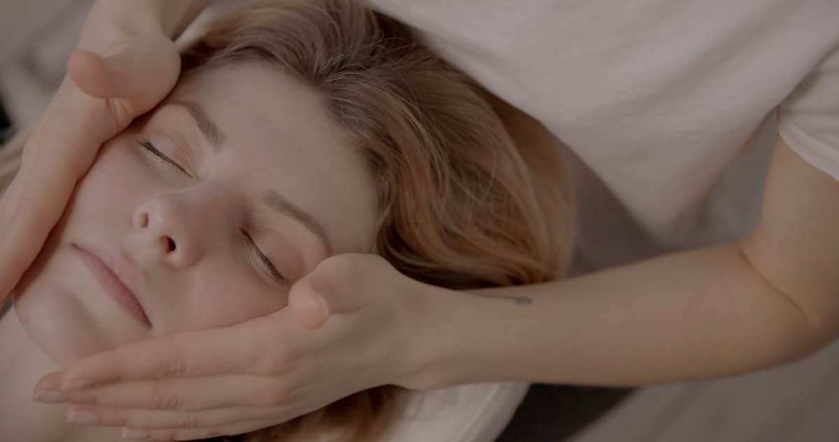 Les mains de l’esthéticienne massent délicatement le visage d’une cliente allongée, les yeux fermés